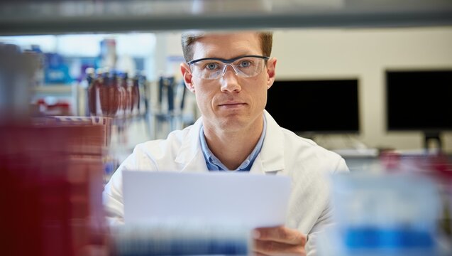 Microbiologist in a crisp white lab coat studies data through clear safety glasses.