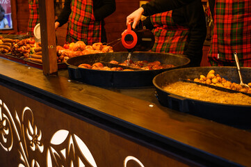 A close shot of street food being served from a large pan at a Christmas market, with festive decor and warm seasonal colors. Ideal for holiday food content, travel blogs, and market advertising.