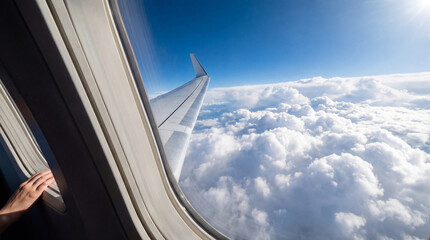 Aerial View of Clouds and Airplane Wing through Window with Passenger Hand