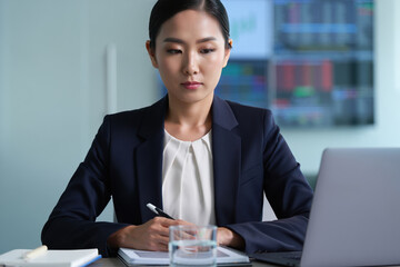 Professional female financial analyst reviews documents at a modern office desk.