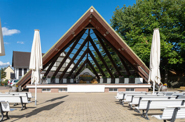 Obraz premium Covered open-air stage with white benches in Burg, Spreewald, Germany. A well-maintained event space surrounded by greenery, typical for festivals and concerts
