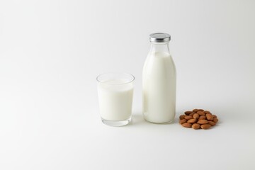 Glass of milk beside a bottle of milk and a pile of almonds on a clean white background, showcasing healthy beverage options and natural ingredients for nutrition
