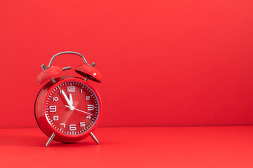 A vibrant red vintage-style alarm clock with twin bells sits on a matching red background, 5 minutes before the New Year. Minimal celebration concept with copy space.