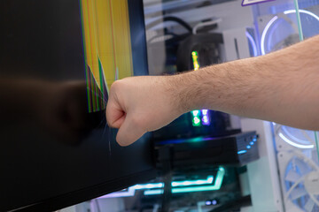 Frustrated gamers fist violently smashes a cracked computer monitor, displaying bright colorful lines, symbolizing technology failure, gaming rage, and digital stress
