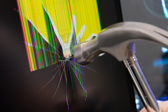 Metal hammer forcefully impacts a monitor screen, causing extensive cracks and vivid, colorful pixel lines, symbolizing technology frustration, damage, or system failure