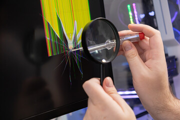 Technician's hands diagnosing a cracked computer monitor display with a magnifying glass and screwdriver, identifying pixel damage for electronics repair