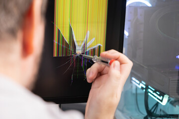 A technician points a screwdriver at a severely cracked computer monitor displaying colorful...