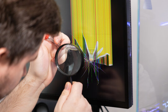 Expert technician carefully examining a severely damaged computer monitor display with a visible cracked screen and vibrant pixel lines for electronic repair