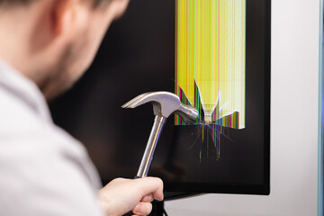 Angry individual smashes a computer monitor screen with a hammer, causing severe cracks and vibrant lines, symbolizing technology frustration