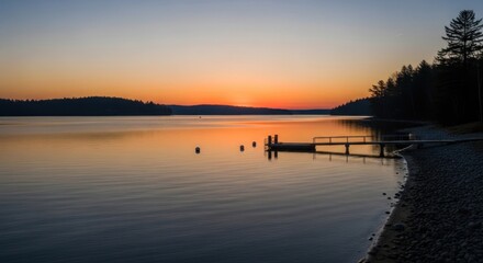 Serene lake water reflects vibrant sunset hues near a wooden dock and forested shoreline