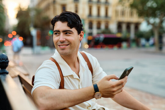Young man enjoys sunny day while using smartphone in urban setting, highlighting his joy and connection to the world around him - Powered by Adobe