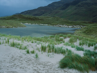 Wind blowing across coastal dune grass, Blue Lagoon, and Mountains Under Moody Sky