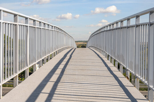 A play of light and shadow is projected onto the pavement, created by the framework of the white structure, in a shot devoid of any human presence