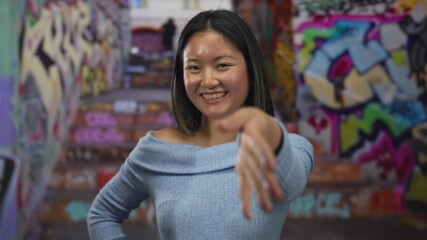 Woman smiling reaching out hand in urban street with colorful graffiti background conveying friendliness warmth and invitation outdoors in city environment