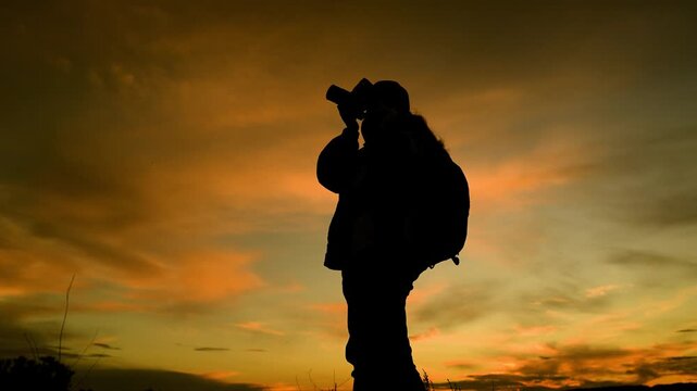 Woman photographer takes photo with camera beautiful landscape at sunset with amazing sky. Woman traveler with camera, backpack, silhouette. Photographer takes beautiful photos of nature at sunrise