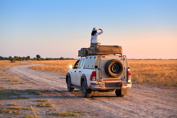 Woman on Rooftop Tent Observing Savannah Landscape from 4x4 Overland Vehicle. © Martin Mecnarowski