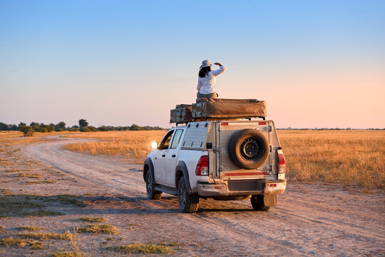 Woman on Rooftop Tent Observing Savannah Landscape from 4x4 Overland Vehicle.