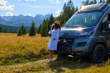 Woman stands by her campervan, enjoying sunny mountain meadow near a forest. Durmitor, Montenegro....