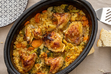 A close view of a baked chicken and vegetable rice dish in a round pot, featuring golden roasted pieces and vibrant ingredients that highlight the warmth and richness of homemade cooking.