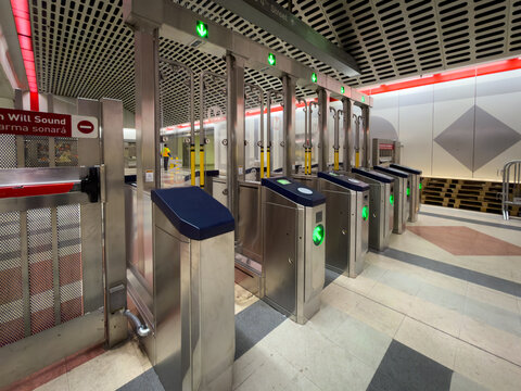 LOS ANGELES, CA, OCT 5, 2025: Side angle of LA Metro fare gates with blue padded surfaces, tap readers, green lights, mesh ceiling with red lighting