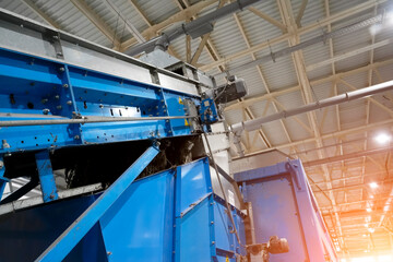 Workers operate large machines in a spacious industrial facility. Equipment efficiently sorts and processes various materials under bright overhead lights