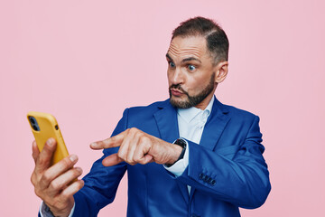A business professional man against a solid pink backdrop, focused on his smartphone, posture...