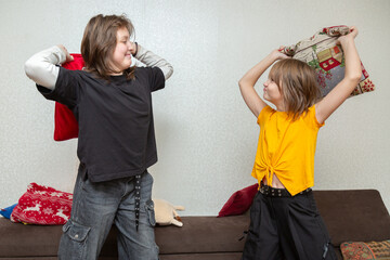 Two young funny girls having pillow fight on the sofa at home