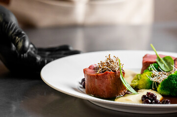 Finely plated beef tenderloin medallions served with broccoli sprouts, a creamy purée, and dark berries at a gourmet restaurant