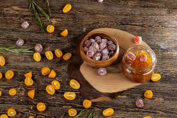 jam made from citrus fruits and dried in sugar syrup, whole kumquat fruits in white powder, a glass jar with sweet orange jam on the table