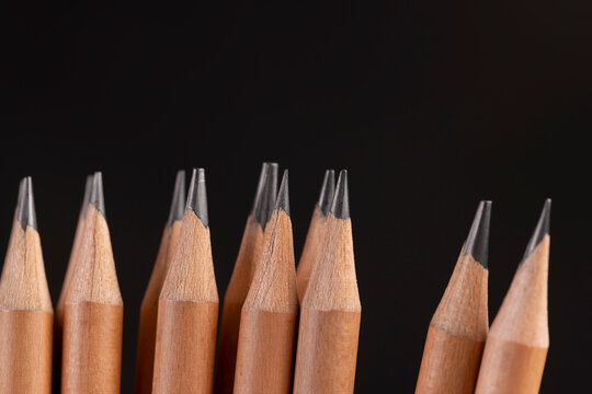 a group of wooden pencils on a black background, stacked pencils made of wood and a lead made of graphite