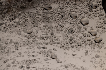 a wet old glass lies on a black slate board with an uneven texture, a whole sheet of transparent glass used in construction covered with water droplets