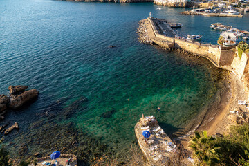 Obraz premium Aerial view of Mermerli Beach's turquoise waters and rocky shore near Kaleici marina. A few swimmers and sunbathers enjoy the sunny winter day in Antalya, Turkey, Mediterranean.