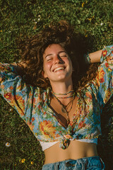 Cheerful young woman lying on green grass, smiling with eyes closed and enjoying the sunlight in a relaxed outdoor setting.
