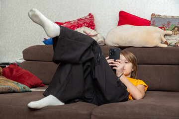 Cute caucasian little girl using modern phone on the sofa at home