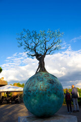 Tree Sculpture on Blue Sphere: Public Art Installation in Open Plaza Under Clear Sky