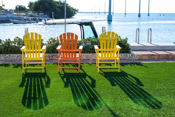 three Adirondack chairs colors yellow and orange on terrace by the ocean on sunny day