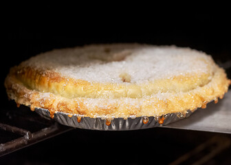 Close-up of a rustic, raw dough cherry pie, glistening with a sugar topping, being slid into a hot dark oven to begin baking in the cafe.