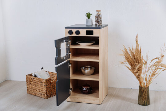 Wooden toy kitchen cabinet with open doors and shelves in minimalist kids room
