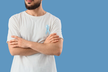 Young man with blue ribbon on color background. Prostate cancer awareness concept