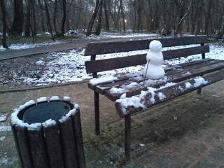 Small Snowman Sitting Alone on a Park Bench in an Early Winter Landscape with Bare Trees at Dusk_2