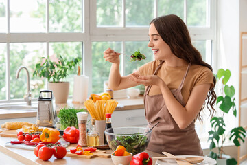 Young woman eating vegetable salad at table in kitchen