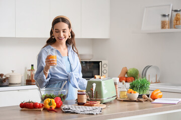 Young woman with juice making toasts in kitchen