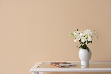 Vase with beautiful lily flowers and magazine on glass coffee table near beige wall