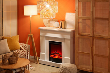 Fototapeta premium Fireplace with sofa, closet and glowing lamps near orange wall in living room