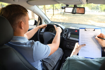 Young man with instructor passing driving license test in car, back view