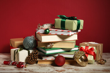 Books with Christmas balls and gift boxes on white wooden table against red background