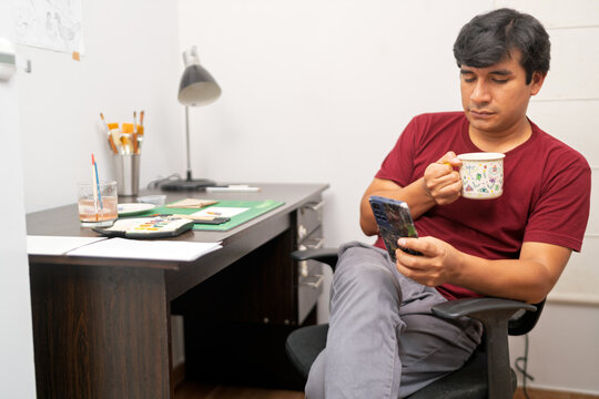 Visual artist relaxing with coffee and smartphone in studio - Powered by Adobe