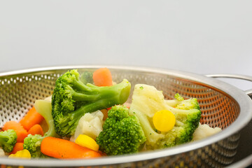 Steamed mixed vegetables in metal colander, closeup