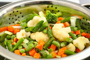 Frozen mixed vegetables steaming in metal colander, closeup
