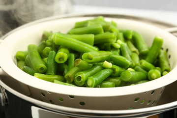 Frozen green beans steaming in colander over pot, closeup